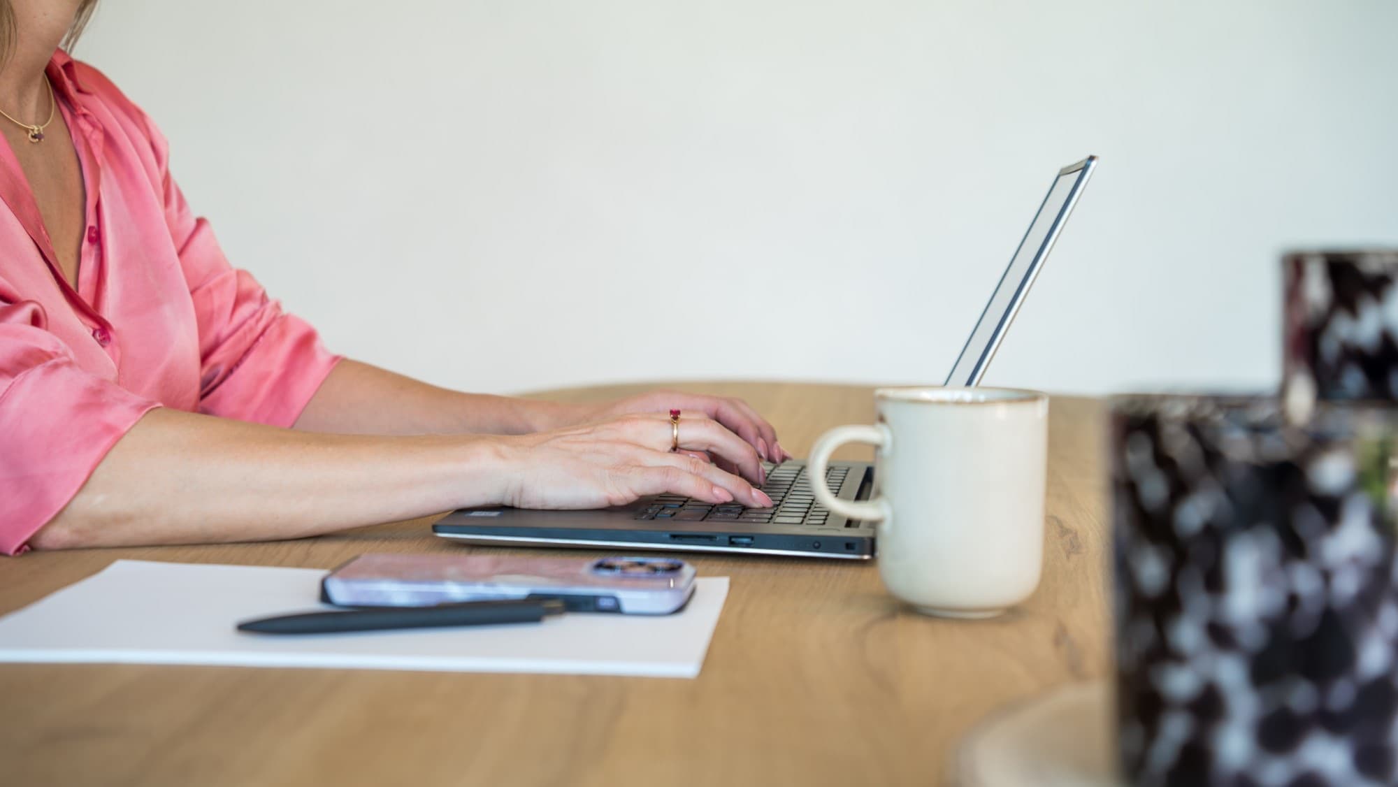 Handen op een laptop naast een koffiemok